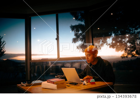 A Focused Young Individual Working Late Amidst a Scenic Sunset Sky A Focused Young Individual Working Late Amidst a Scenic Sunset Sky 134393678