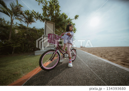A Child Delightfully Enjoying a Joyful Day on a Bright Pink Bicycle by the Beach 134393680
