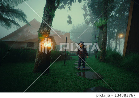 Child Walking on Pathway in Foggy Forest with Tents and Lanterns Child Walking on Pathway in Foggy Forest with Tents and Lanterns 134393767