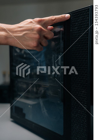 Close-up of technician finger pointing at layer of dust accumulated on glass panel of computer case. Concept of importance of regular cleaning for optimal performance and longevity. 134393793