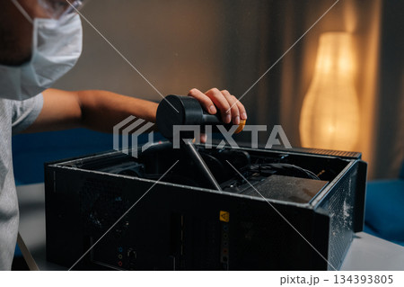 Closeup of technician in face mask and safety glasses cleaning computer case using small vacuum cleaner, demonstrating proper maintenance procedures. Concept of service, repair and cleaning computer Closeup of technician in face mask and safety glasses cleaning computer case using small vacuum cleaner, demonstrating proper maintenance procedures. Concept of service, repair and cleaning computer 134393805