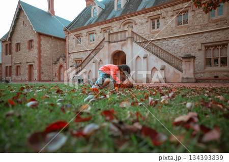 young child investigating leaves outdoors, child examining leaves near stone building 134393839