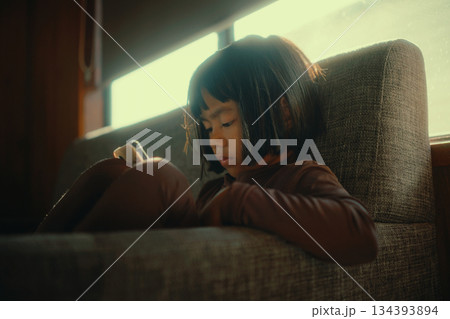 A Thoughtful Child is Comfortably Sitting on a Couch with a Mobile Device A Thoughtful Child is Comfortably Sitting on a Couch with a Mobile Device 134393894