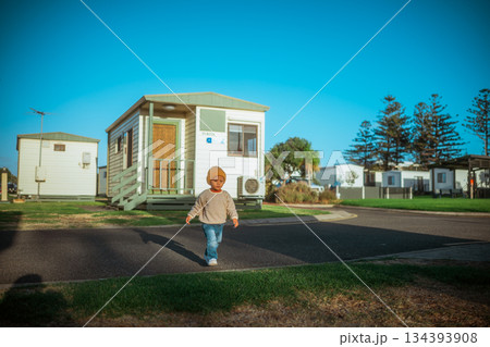 boy races between mobile homes, caucasian toddler in beanie dashes through sunny mobile boy races between mobile homes, caucasian toddler in beanie dashes through sunny mobile 134393908