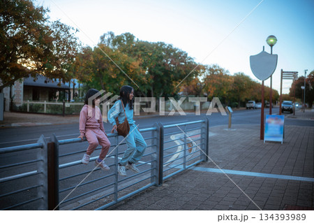 Two Children Happily and Playfully Sitting on a Fence Together at Dusk as the Sun Sets Two Children Happily and Playfully Sitting on a Fence Together at Dusk as the Sun Sets 134393989