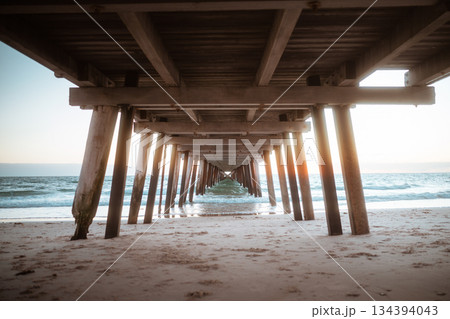 serene pier by sunrise, pier with wooden posts leading to glowing sunrise over ocean 134394043