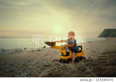 A Young Child Joyfully Playing with a Colorful Toy Truck at Sunset on the Beautiful Beach 134394070