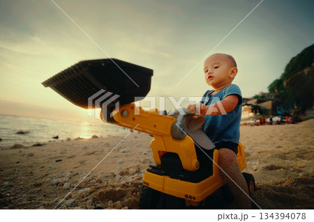 A Little Child Joyfully Playing with a Colorful Toy Dump Truck on the Beach at Sunset A Little Child Joyfully Playing with a Colorful Toy Dump Truck on the Beach at Sunset 134394078