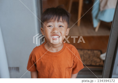 A Smiling and Joyful Young Boy Standing at His Home Doorway with Cheer A Smiling and Joyful Young Boy Standing at His Home Doorway with Cheer 134394172