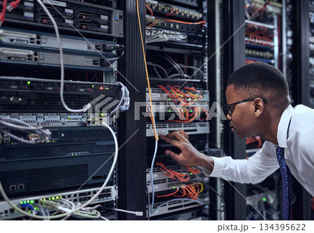 Black man, IT technician and server room for cyber security, data or network storage inspection. African male person or networking administrator checking system, cables or installation at datacenter Black man, IT technician and server room for cyber security, data or network storage inspection. African male person or networking administrator checking system, cables or installation at datacenter 134395622