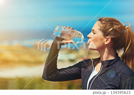 Woman drinking water, health and fitness in nature, blue sky and athlete outdoor with hydration and mockup space. Exercise at beach, female person drink h2o in bottle, workout and break from training 134395623
