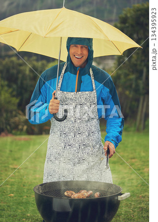 Happy man, portrait and umbrella in rain for barbecue meal, supper or dinner on the fire grill. Male person smiling for insurance, cover or protection while cooking under raining or stormy weather Happy man, portrait and umbrella in rain for barbecue meal, supper or dinner on the fire grill. Male person smiling for insurance, cover or protection while cooking under raining or stormy weather 134395923