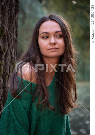 A thoughtful portrait of a woman standing by a tree near calm water, with soft light, natural tones, and a serene, reflective mood A thoughtful portrait of a woman standing by a tree near calm water, with soft light, natural tones, and a serene, reflective mood 134396438