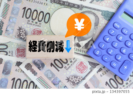 経費削減を示す木ブロックと電卓と日本円のイメージ。 経費削減を示す木ブロックと電卓と日本円のイメージ。 134397055