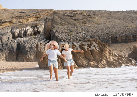 Happy girls running in sea water on beach during Happy girls running in sea water on beach during 134397997