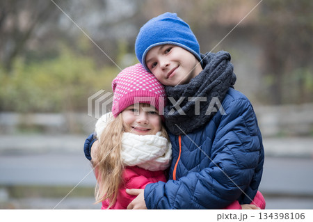 Two children boy and girl hugging each other outdoors wearing warm clothes in cold autumn or winter weather. Two children boy and girl hugging each other outdoors wearing warm clothes in cold autumn or winter weather. 134398106