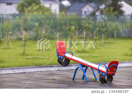 Seesaw swing in big yard with soft rubber flooring on sunny summer day. 134398197