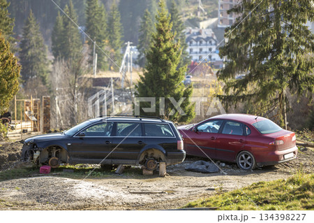 Red car parked in recreation zone and old rusty broken trash car after crash accident without wheels on wood stamps on sunny day outdoors abandoned on blurred resort construction site background. Red car parked in recreation zone and old rusty broken trash car after crash accident without wheels on wood stamps on sunny day outdoors abandoned on blurred resort construction site background. 134398227