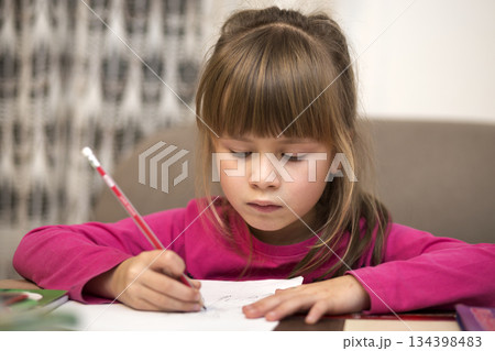 Portrait of cute pretty little serious child girl drawing with pencil on paper on blurred background. Art education, creativity, doing homework and children activities concept. Portrait of cute pretty little serious child girl drawing with pencil on paper on blurred background. Art education, creativity, doing homework and children activities concept. 134398483