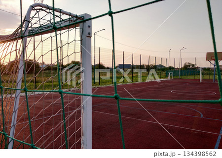 Outdoors mini football and basketball court with ball gate and basket surrounded with high protective fence. 134398562