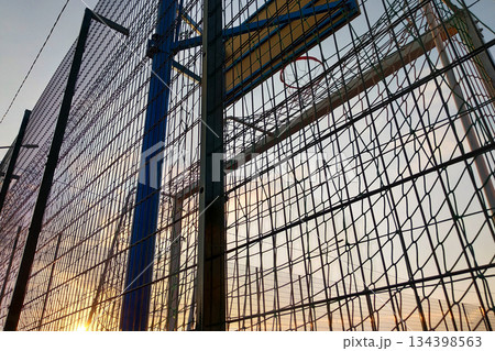 Outdoors mini football and basketball court with ball gate and basket surrounded with high protective fence. 134398563