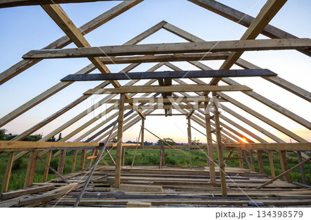 New wooden house under construction. Close-up of attic roof frame against clear sky from inside. Ecological dream home of natural materials. Building, construction and renovation concept. New wooden house under construction. Close-up of attic roof frame against clear sky from inside. Ecological dream home of natural materials. Building, construction and renovation concept. 134398579