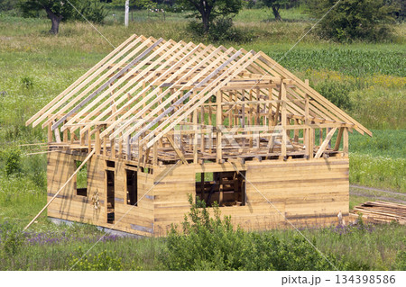 New wooden cottage of natural lumber materials with steep plank roof frame under construction in green neighborhood. Property, investment, professional building and reconstruction concept. New wooden cottage of natural lumber materials with steep plank roof frame under construction in green neighborhood. Property, investment, professional building and reconstruction concept. 134398586