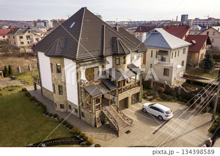 New expensive white car parked in paved well-kept yard with green lawn, decorative bushes and brick fence of big two story house. Luxury and prosperity concept. 134398589