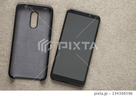 New black modern cellphone and plastic protective case isolated on light cloth copy space background. Modern technology, communication, gadget design and accessories concept. New black modern cellphone and plastic protective case isolated on light cloth copy space background. Modern technology, communication, gadget design and accessories concept. 134398596