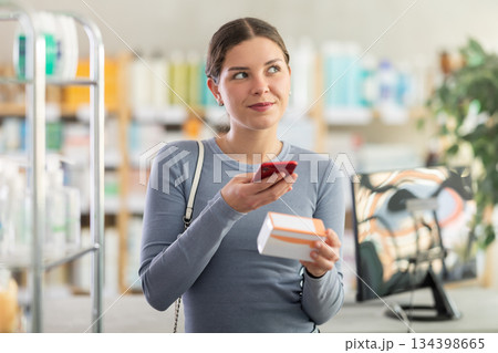 Female shopper in pharmacy scanning barcode on box of pills with smartphone 134398665