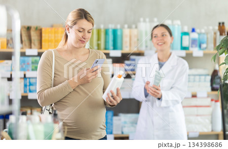 Pregnant woman buyer scans cream qr code with woman pharmacist Pregnant woman buyer scans cream qr code with woman pharmacist 134398686