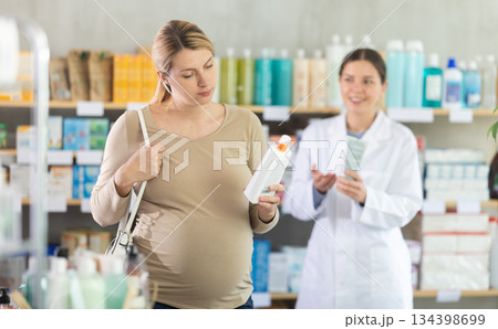 Pregnant woman choose diaper rash cream in pharmacy, pharmacist in background offer similar product 134398699
