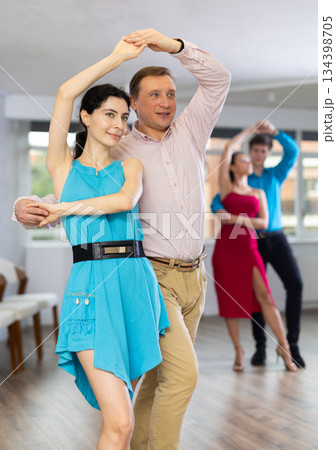 Smiling brunette in blue dress practicing bachata with male partner Smiling brunette in blue dress practicing bachata with male partner 134398705