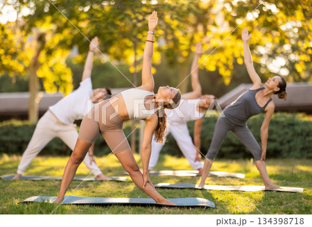 Girl enjoying group yoga session on green glade 134398718