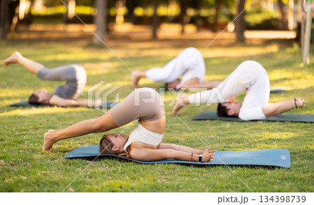 Yoga lesson visitors with coach perform plow pose in park Yoga lesson visitors with coach perform plow pose in park 134398739