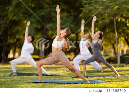 Girl performing Baddha Viparita Virabhadrasana during group yoga Girl performing Baddha Viparita Virabhadrasana during group yoga 134398740