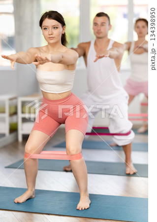 Young girl practicing half squat with band standing on mat 134398950