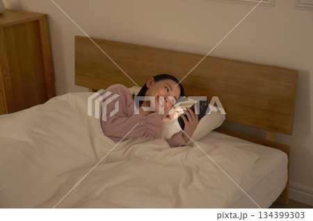 布団の中でスマホを使う女性 134399303