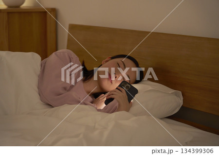 布団の中でスマホを使いながら寝落ちする女性 134399306