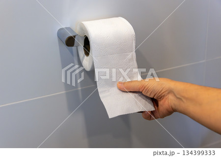 Close up of woman hand pulling toilet paper in holder. Close up of woman hand pulling toilet paper in holder. 134399333