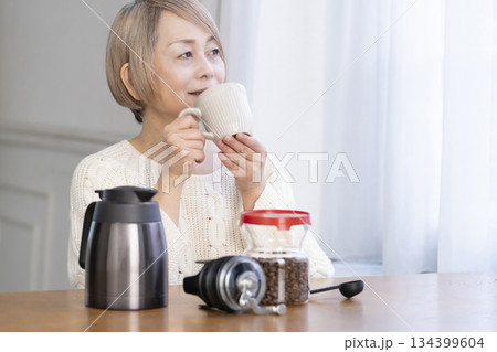 リビングでコーヒー豆を挽いてコーヒーを飲んで寛ぐシニア女性 134399604