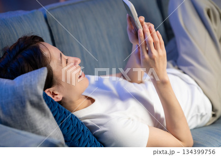 ソファーに寝そべりスマホを見る女性 ソファーに寝そべりスマホを見る女性 134399756