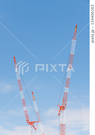 3基の赤白に塗装された建設用クレーンと青空 134400163