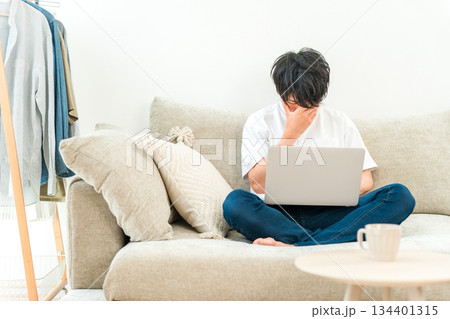リビングのソファーでパソコンを使う男性(ショック,落ち込む,失敗,ミス,どうしよう,後悔) リビングのソファーでパソコンを使う男性(ショック,落ち込む,失敗,ミス,どうしよう,後悔) 134401315