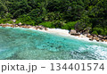 A calm beachfront with shallow turquoise waters and a backdrop of lush greenery. La Digue, Seychelles. 134401574