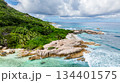 Waves break over granite rocks along a coastline fringed by lush greenery and clear waters. Seychelles, La Digue. 134401575
