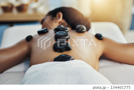 Woman, relax and stone massage at spa for skincare, beauty or body treatment on bed at resort. Calm female lying in relaxation with hot rocks or pile on back in therapy, zen or wellness at salon 134401775