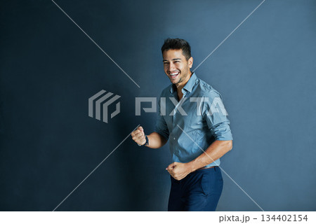 Celebration, fist pump and portrait of a businessman in a studio with achievement or winning. Happy, smile and professional male employee winner with success to celebrate isolated by blue background. 134402154