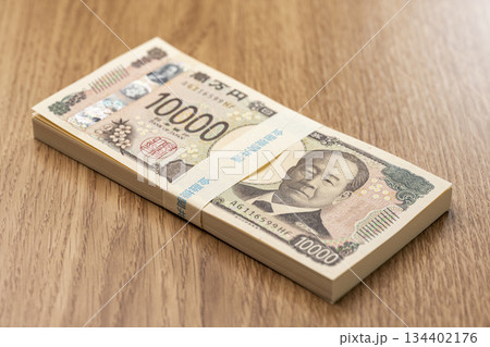 木目テーブルに置かれた百万円の一万円札束が象徴する日本円の高額資金 134402176
