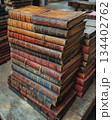 Stacked vintage leather-bound books resting on an antique wooden table in a cozy library setting. Generative AI 134402762